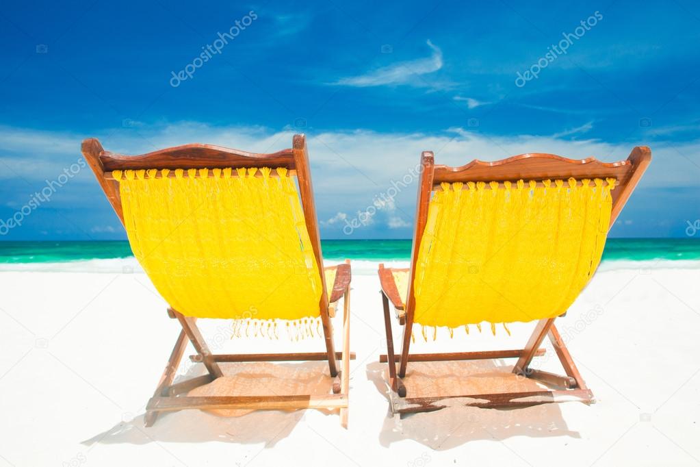 two yellow beach chairs and umbrella on sand beach. Holidays