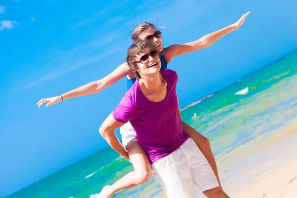 Coppia felice in occhiali da sole in vacanza a cavalluccio allegro sulla spiaggia — Foto Stock