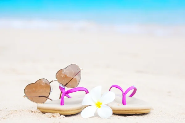 Klapki japonki, okulary w kształcie serca i frangipani na tropikalnej plaży — Zdjęcie stockowe