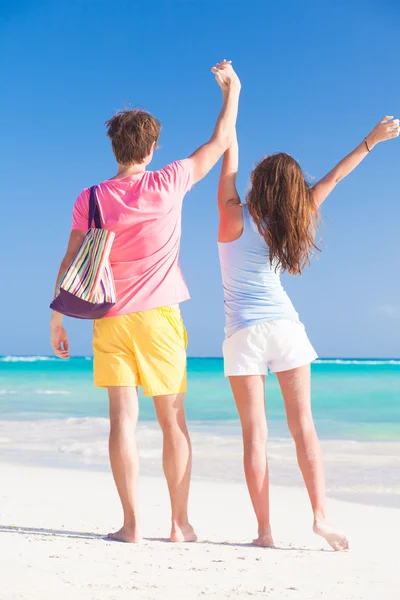 Visão traseira de feliz jovem casal sendo alegre na praia. mãos para cima — Fotografia de Stock