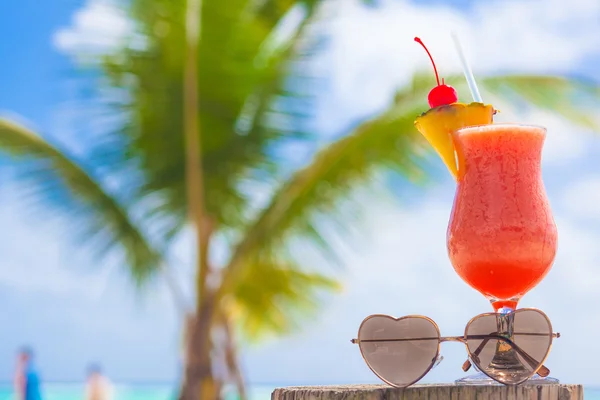 Copo de cocktail de frutas e óculos de sol em forma de coração na mesa perto da praia — Fotografia de Stock