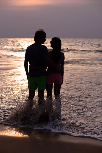 Zonsondergang silhouet van jong paar in liefde knuffelen op het strand — Stockfoto