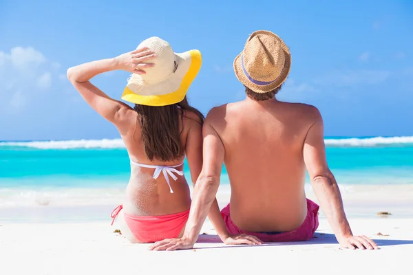 Feliz jovem casal em chapéus sentado em uma praia tropical em Barbados — Fotografia de Stock