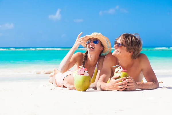 Feliz joven pareja acostada en una playa tropical en Barbados y bebiendo un cóctel de coco —  Fotos de Stock