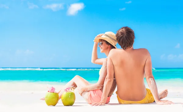 Happy young couple lying on a tropical beach in Barbados and drinking a coconut cocktail — Stock Photo, Image