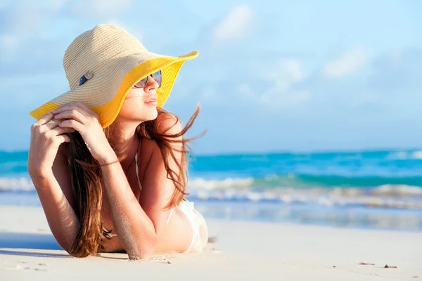 Frau im Bikini und Strohhut am Tropenstrand liegend lizenzfreie Stockbilder
