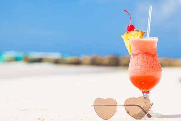 Glass of fruit cocktail  and heart shaped sunglasses on table near the beach — Stock Photo, Image