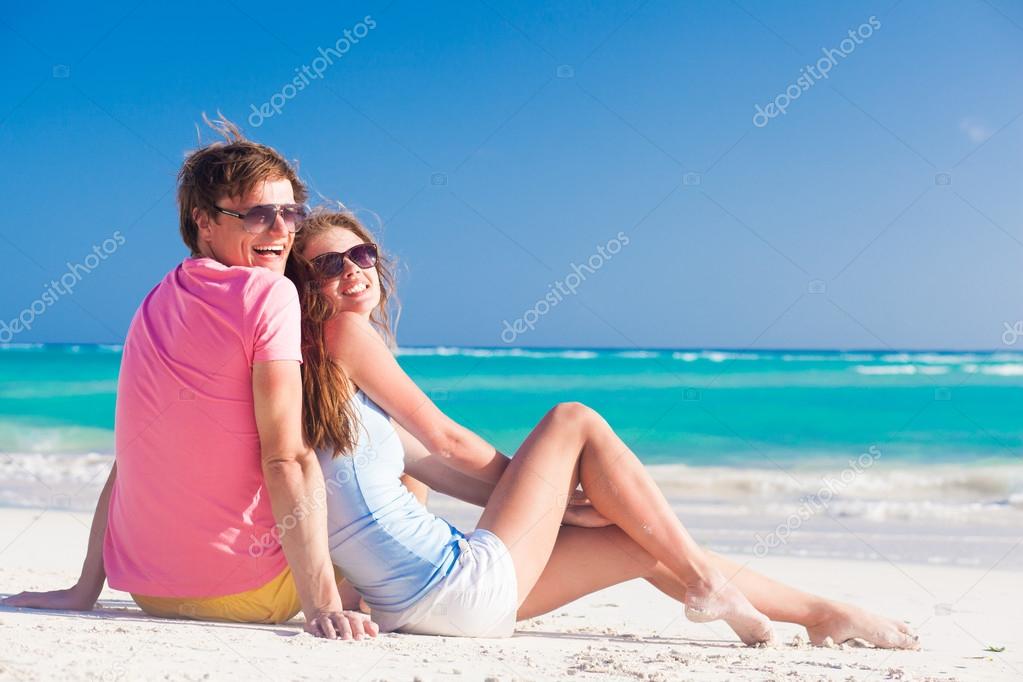 Closeup of happy young caucasian couple in sunglasses smiling on beach and looking at sun