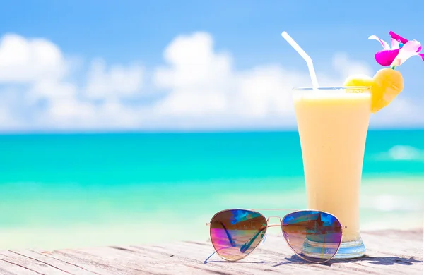 Imagen de plátano fresco y jugo de piña y gafas de sol en la playa tropical —  Fotos de Stock