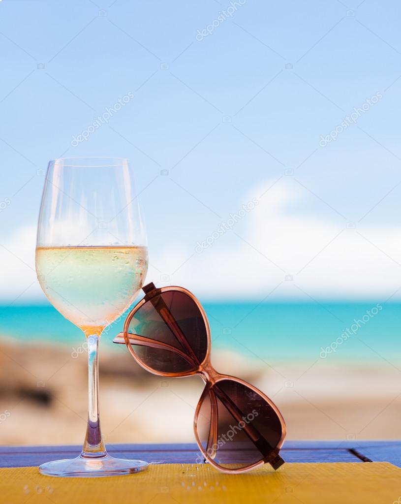 glass of chilled white wine and sunglasses on table near the beach