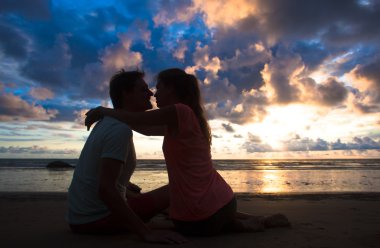 sunset silhouette of young couple in love hugging and kissing at beach