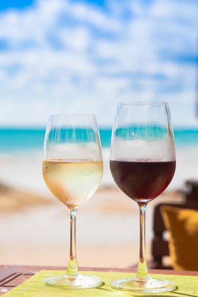 два бокала охлажденного белого и красного вина на столе возле пляжа
