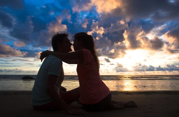 Sunset silhouette of young couple in love hugging and kissing at beach — Stock Photo, Image