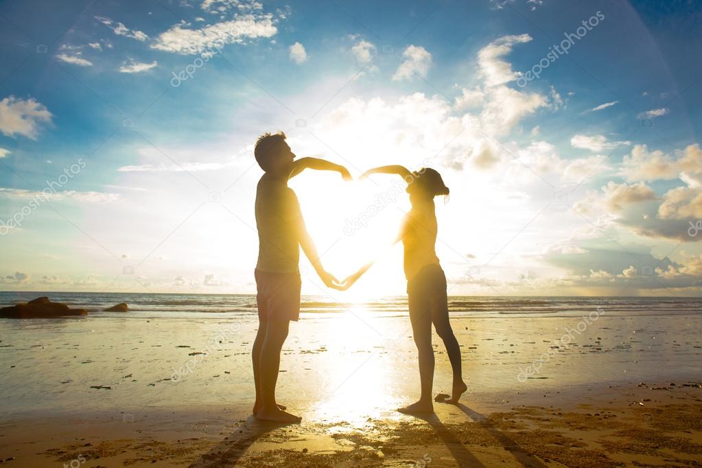 sunset silhouette of young couple in love holding hands at beach