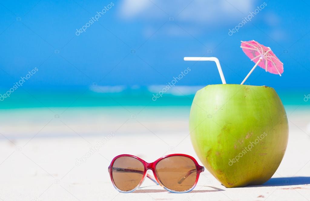 picture of fresh coconut cocktail and blue sunglasses on tropical beach