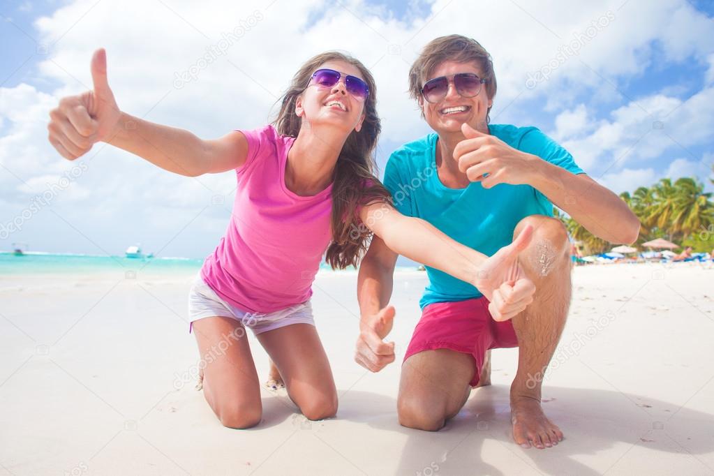 Closeup of happy young caucasian couple in sunglasses smiling on beach. thumbs up 