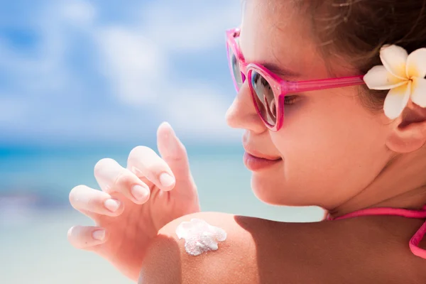 Close up de jovem mulher em óculos de sol colocando creme solar no ombro — Fotografia de Stock