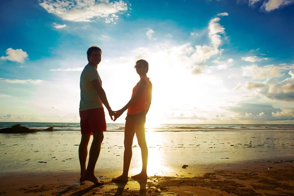 Silhouette tramonto di giovane coppia innamorata che si tiene per mano in spiaggia — Foto Stock