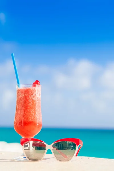 Glass of fruit cocktail and glam sunglasses on table near the beach — Zdjęcie stockowe