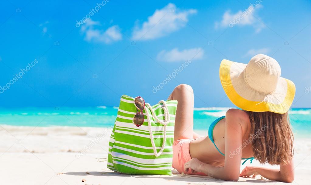 back view of a woman with stripy bag and straw hat lying on beach