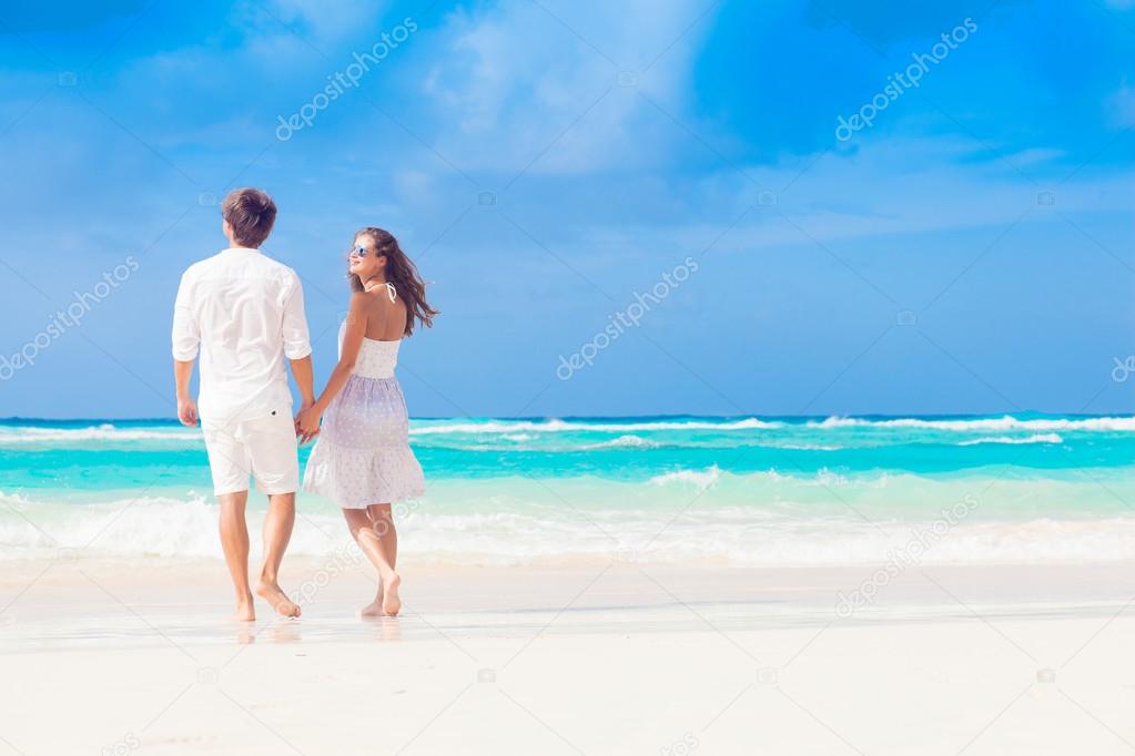 back view of happy romantic young couple walking at the beach