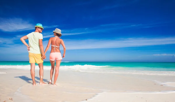 Вид сзади на пару в яркой одежде, держащихся за руки на тропическом пляже — стоковое фото