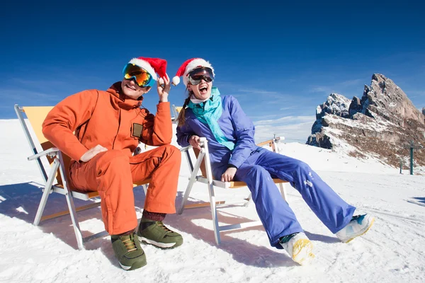 Två snowboardåkare på toppen av berget har roligt sitter på stol schäslong i santa hattar — Stockfoto