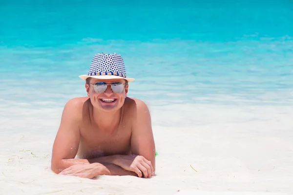 Young man in straw hat and sunglasses lying at tropical beach — Stock Photo, Image