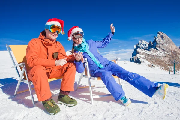Two snowboarders on top of the mountain having fun sitting on chair chaise lounge in santa hats — Stock Photo, Image