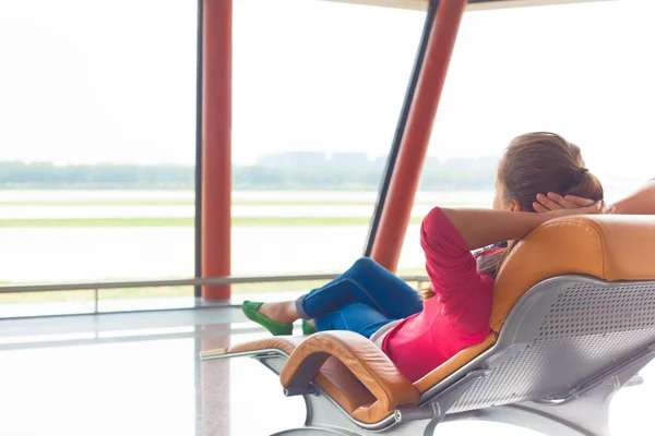 Frau wartet am Flughafen auf Liegestuhl auf ihren Flug — Stockfoto