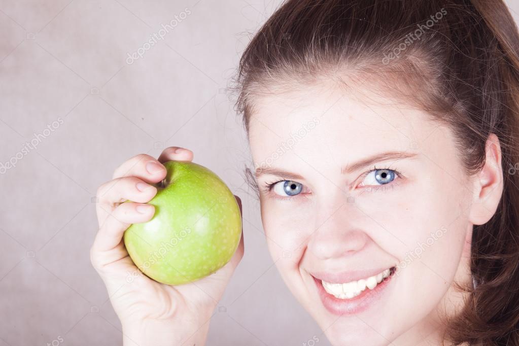 blue eyed young woman smiling with green apple in hand