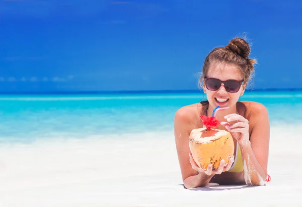Young woman smiling lying in straw hat in sunglasses with coconut on beach — Stock Photo, Image