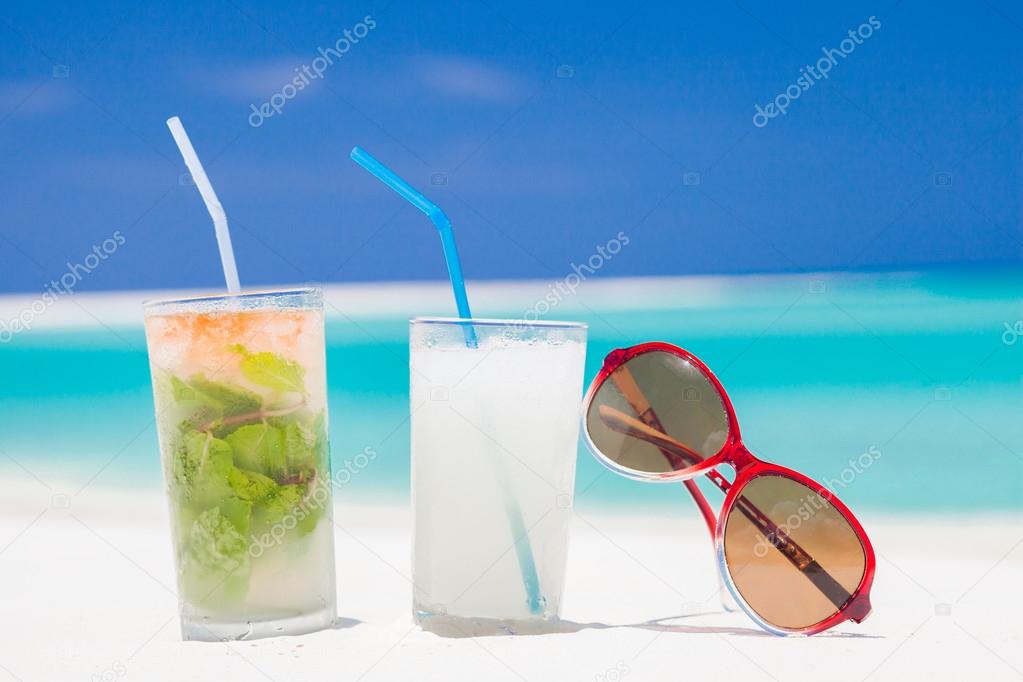 two glasses of chilled cocktail mohito pina colada and sunglasses on a sand beach