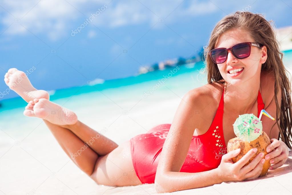 atrractive long haired woman in red swim suit relaxing at tropical beach enjoying her coconut shake