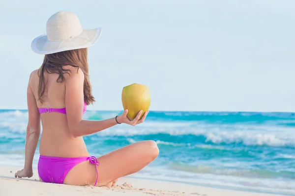 Atractiva mujer de pelo largo en traje de baño rojo relajante en la playa tropical disfrutando de su batido de coco —  Fotos de Stock