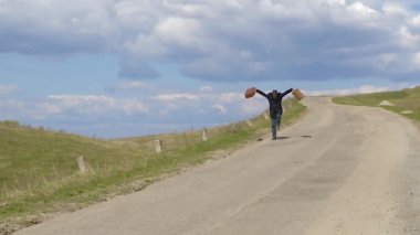 İki eski çanta ile yol boyunca yaz aylarında çim üzerinde yürüyen adam