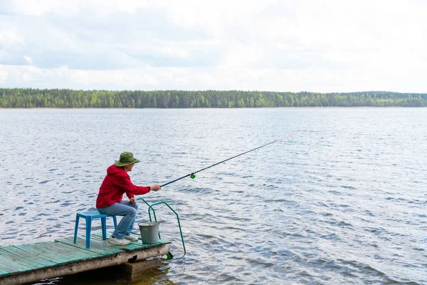 一个拿着帽子和钓竿的渔夫坐在河岸上 — 图库照片
