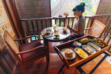 Kadın balkonda nefis bir kahvaltıdan hoşlanıyor, güne mükemmel bir başlangıç. Bali, Endonezya