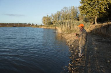 Nehir kenarında duran ve balık tutmaya çalışan bir balıkçı. Spor, eğlence, yaşam tarzı..