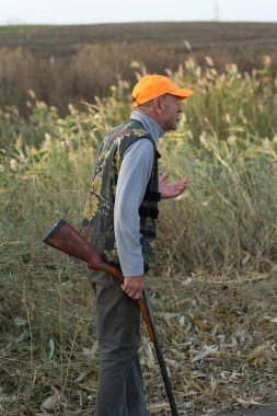 Av tüfeğiyle çayırda yürüyen sülün avcısı..