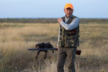 Av tüfeğiyle çayırda yürüyen sülün avcısı..