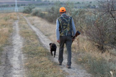 Av tüfeğiyle çayırda yürüyen sülün avcısı..