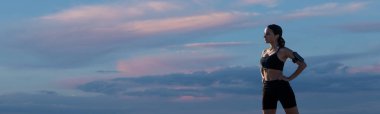 Gökyüzü arka planında spor kıyafetleriyle poz veren kadın. Vücudun orta kısmı..