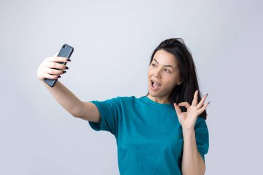 Gri arka planda izole edilmiş selfie çeken güzel bir kızın portresi.