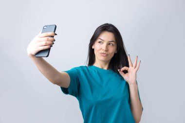 Gri arka planda izole edilmiş selfie çeken güzel bir kızın portresi.