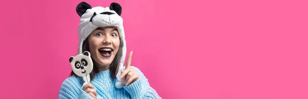 可爱的小女孩站在那里 手里拿着美味的熊猫棒棒糖 头上顶着一顶粉色背景的帽子 — 图库照片