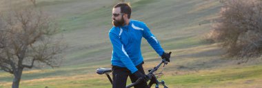 Pantolon ve yün ceketli bir bisikletçi. Havalandırma çatallı, modern bir karbon motorlu. Tepedeki adam bisiklete biniyor..