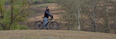 Modern dağ bisikletindeki vahşi sakallı adam. Baharda yeşil tepelerde bisikletçi.