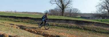 Şortlu ve formalı bisikletçi, modern karbon kuyruklu motorsikletli. Uçurumun kenarında, yeşil bahar ormanlarının arka planında duran bir hava süspansiyon çatalı var.