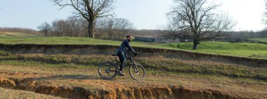 Şortlu ve formalı bisikletçi, modern karbon kuyruklu motorsikletli. Uçurumun kenarında, yeşil bahar ormanlarının arka planında duran bir hava süspansiyon çatalı var.